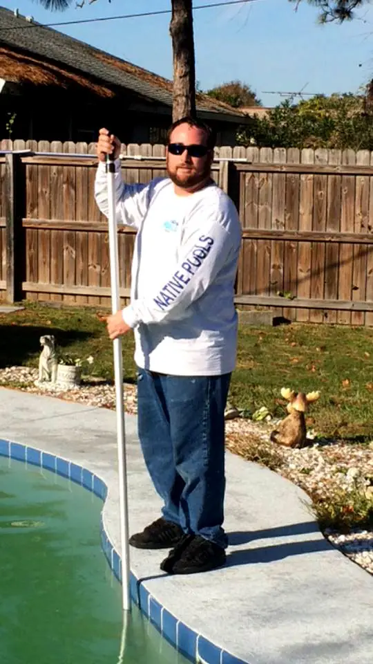 John Sirounis on a pool deck in a Native Pools long-sleeve shirt, pool pole in hand